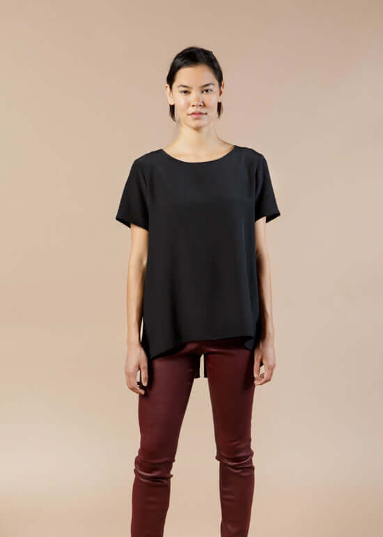 Woman wearing black silk tee top with relaxed fit and high low hem showing front view