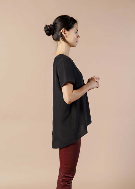 Woman wearing black silk tee top with relaxed fit and high low hem showing side view