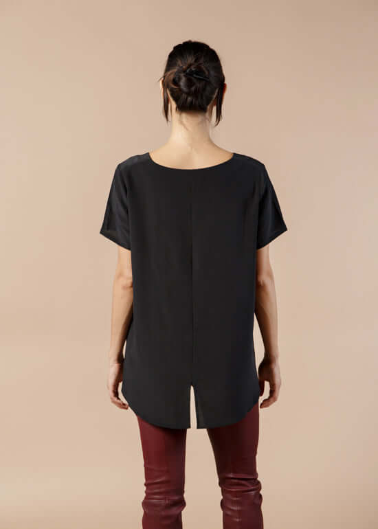 Woman wearing black silk tee top with relaxed fit and high low hem showing back view